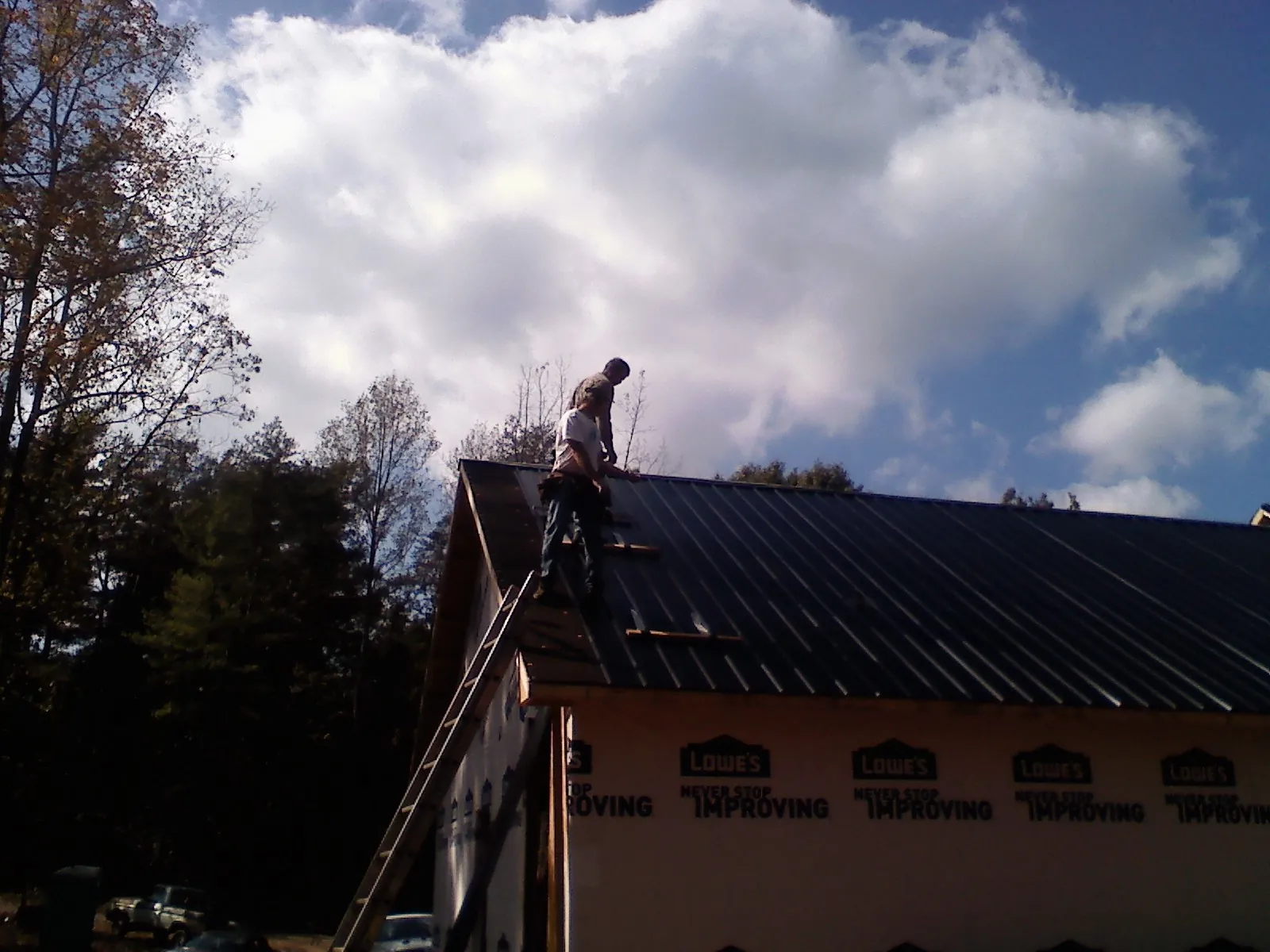 Roofer fastening dark metal panels high against a cloudy sky, from a Roof Inspection job in Lynwood