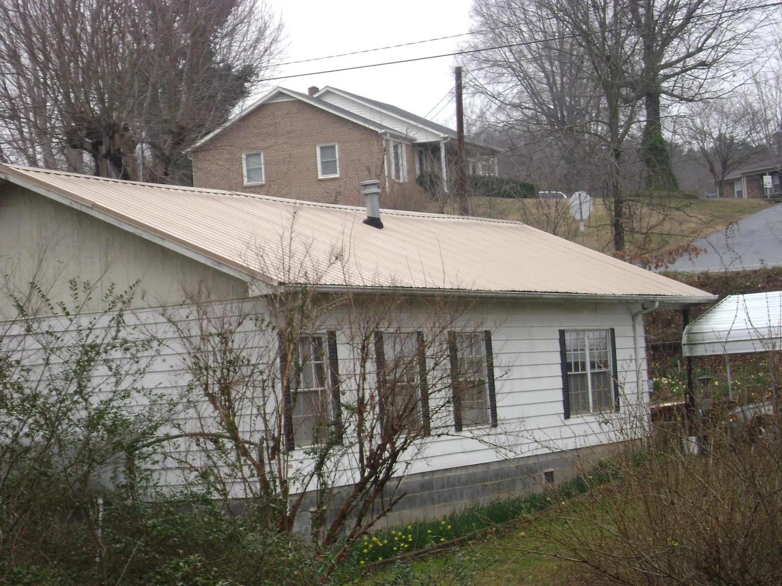 Tan metal roof on a white sided house set into a hillside — Commercial Roofing by Roofing Brothers in Lynwood